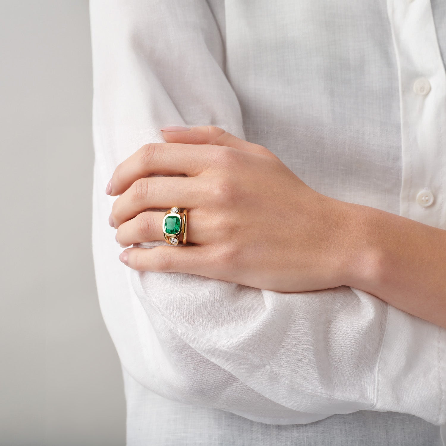 Model wearing handcrafted yellow gold ring featuring a facetted emerald with two round diamonds either side.