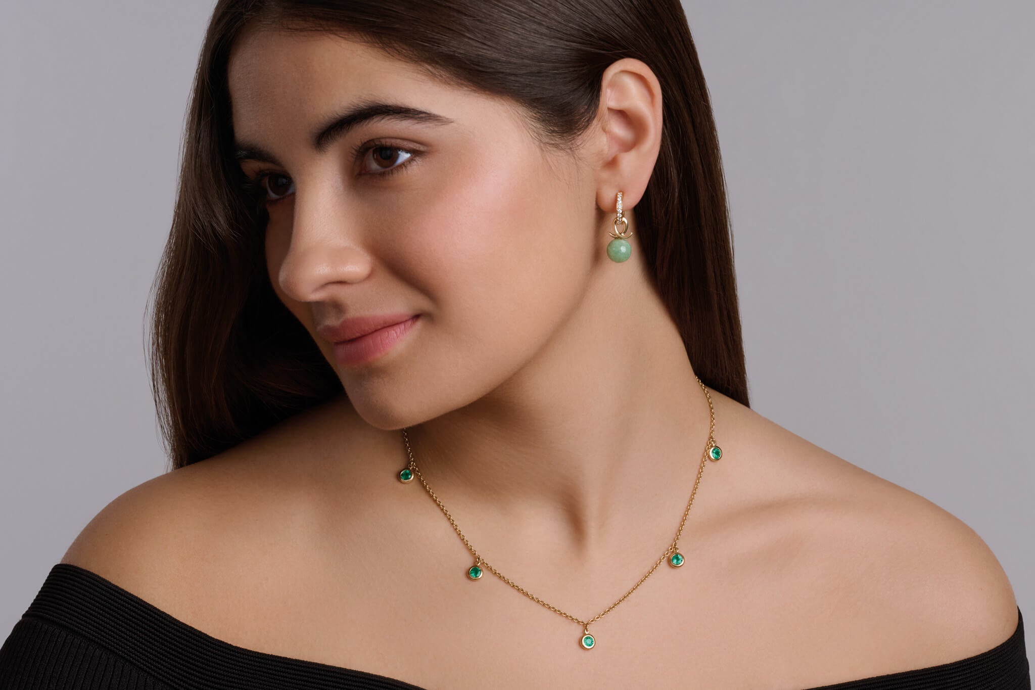 Model wearing handcrafted necklace and earrings in yellow gold and emerald as may birthstone 