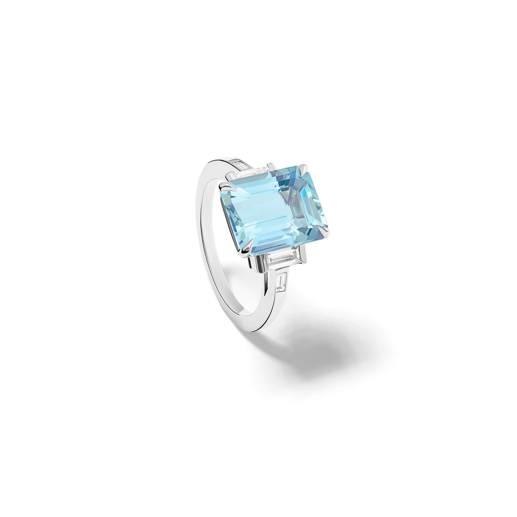 Handcrafted platinum engagement ring featuring a central emerald cut blue aquamarine flanked by two smaller rectangular diamonds on each side, all set in a sleek band.