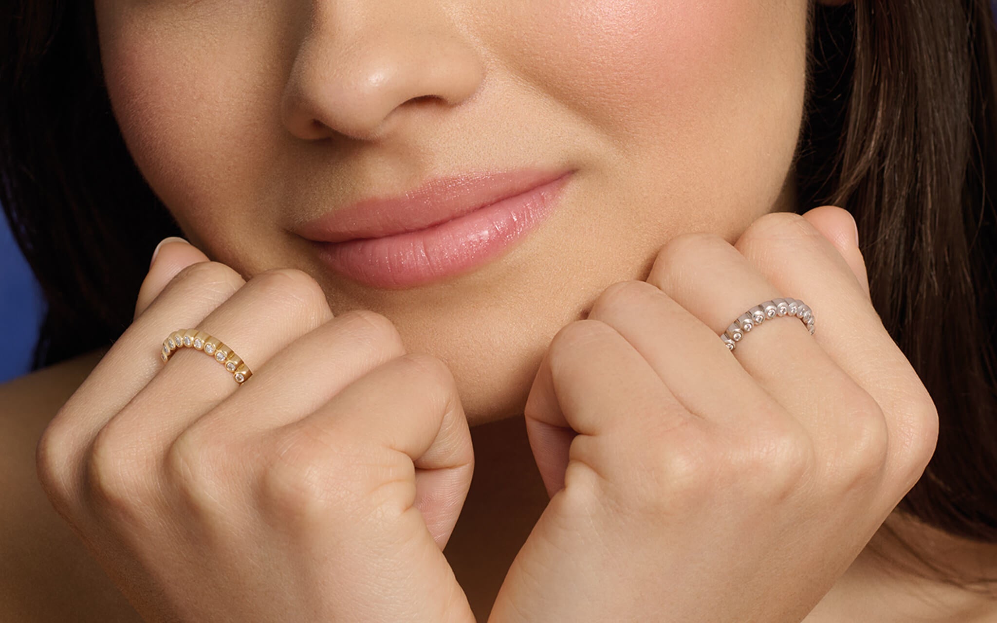 Model posing with both hands on her face wearing Cassandra Goad half eternity rings in yellow and white gold. 