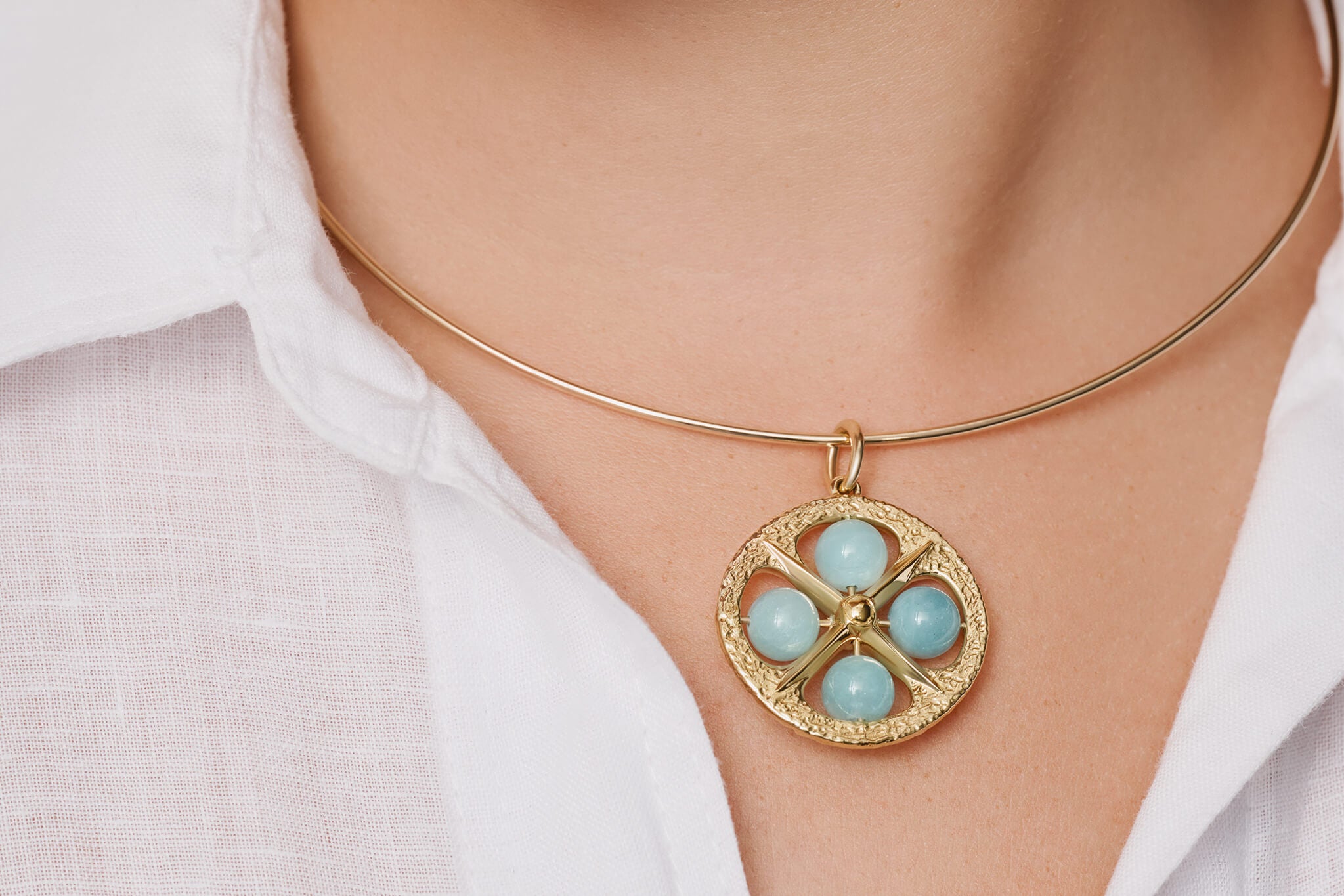 Model wearing a handcrafted yellow gold pendant featuring a beaded aquamarine, birthstone of March.