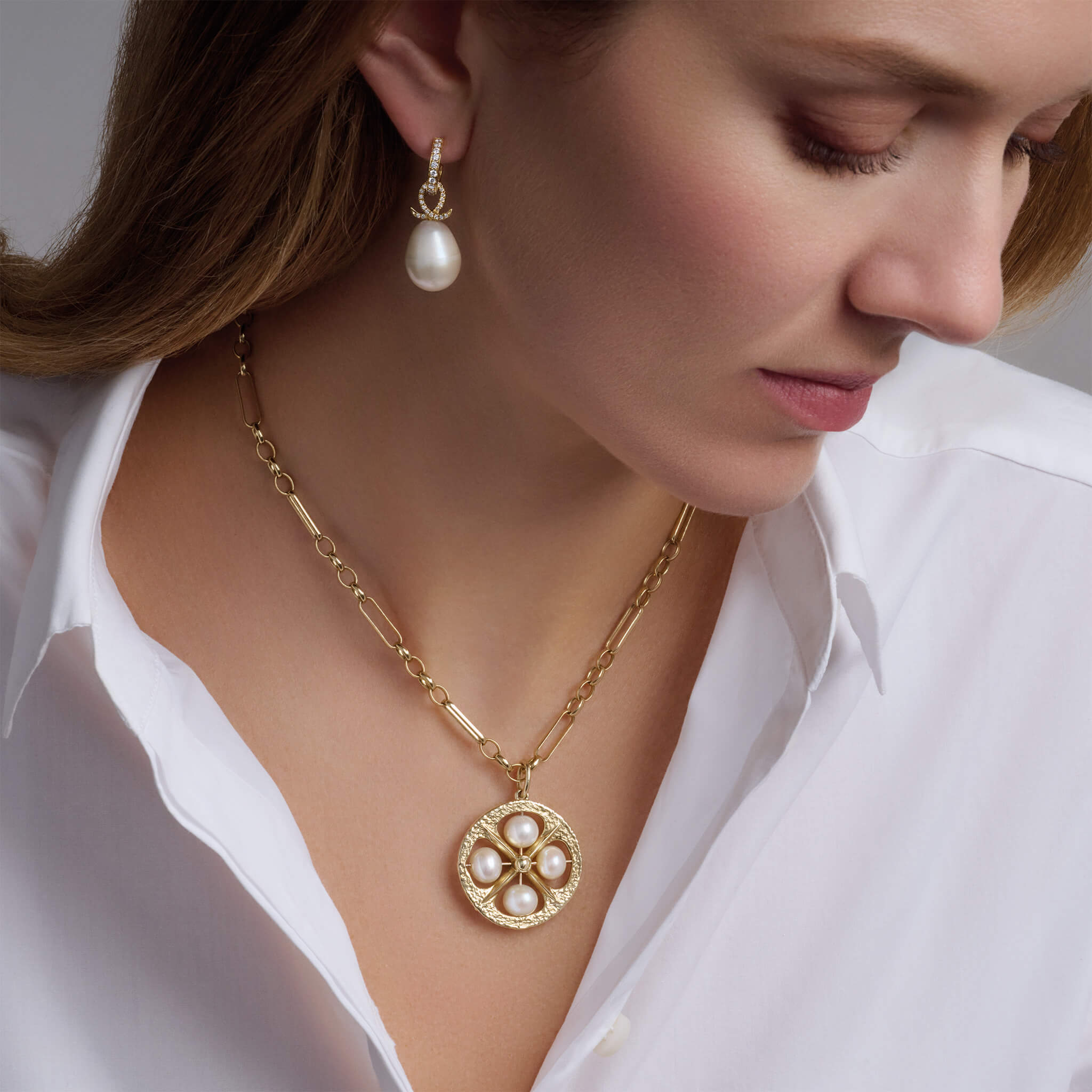 Model wearing handcrafted 9ct yellow gold necklace pendant with a circular motif and a cross in the middle and four pearls.