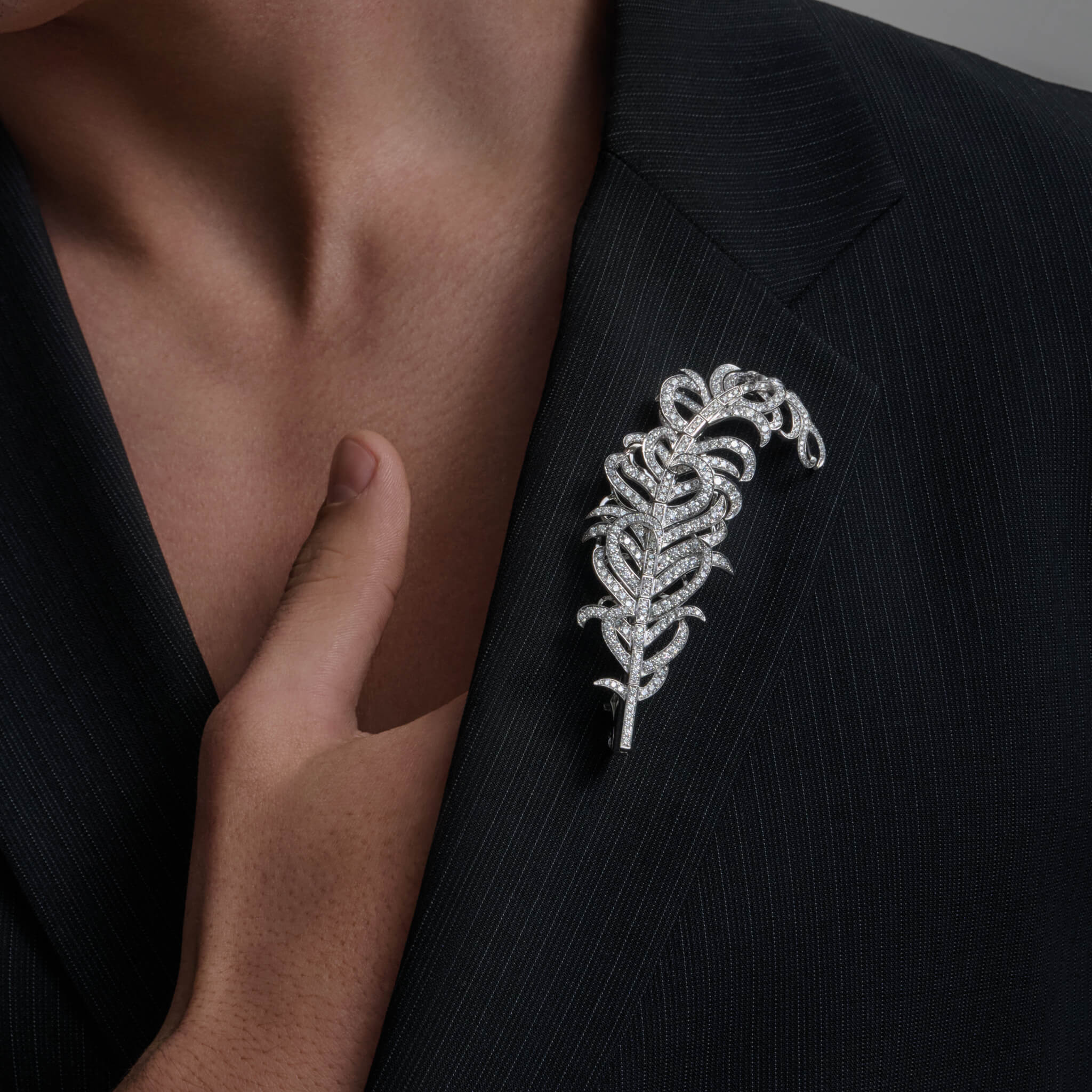model wears handcrafted high jewellery: Feather Plume Masterpiece brooch in 18ct white gold with diamonds, in the shape of a feather.