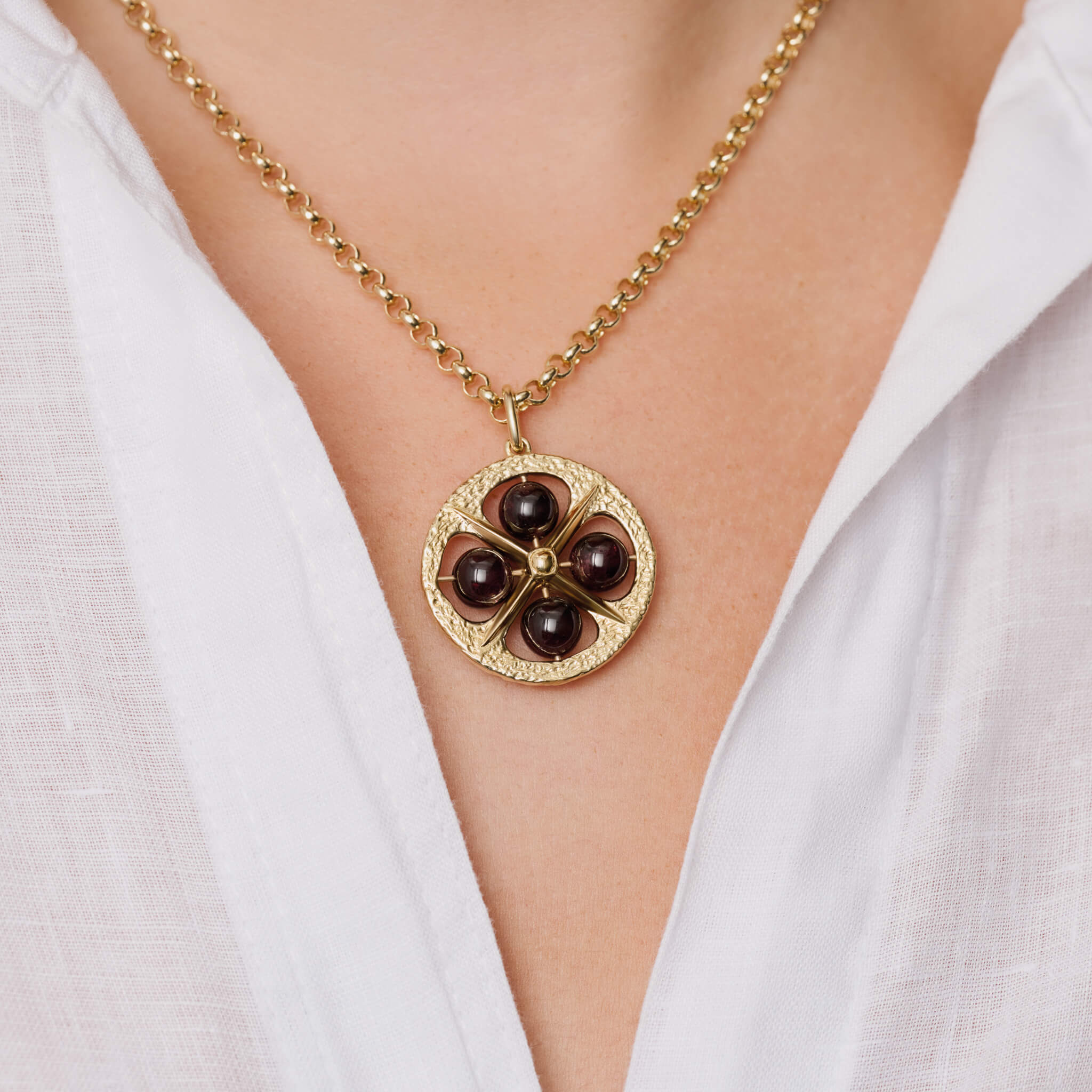 Model wears a handcrafted 9ct yellow gold Helios pendant with four red garnet beads, the birthstone for January.