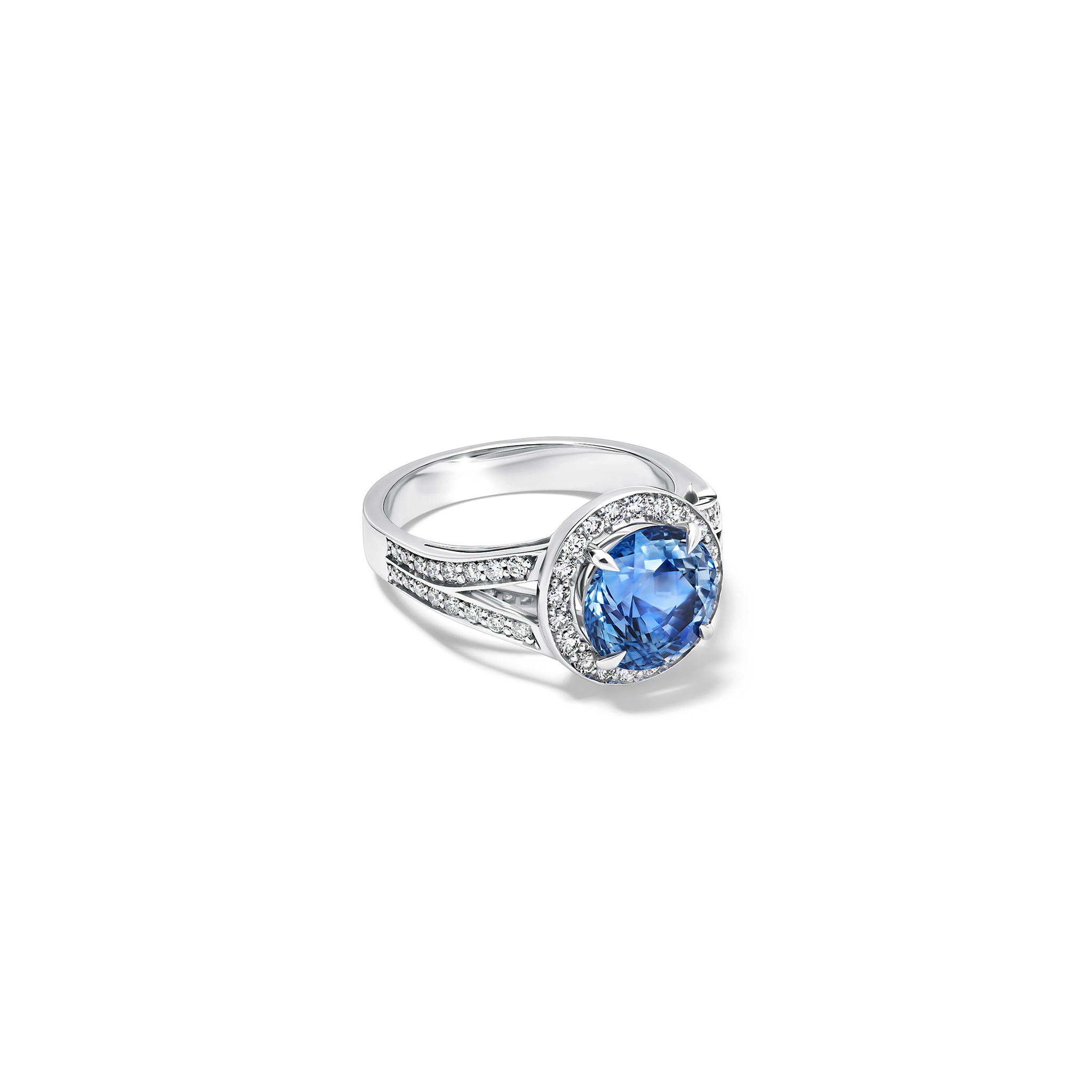 Handcrafted 18ct white gold engagement ring with a large round central blue sapphire surrounded by a halo of small diamonds and smaller diamonds embedded along the band.