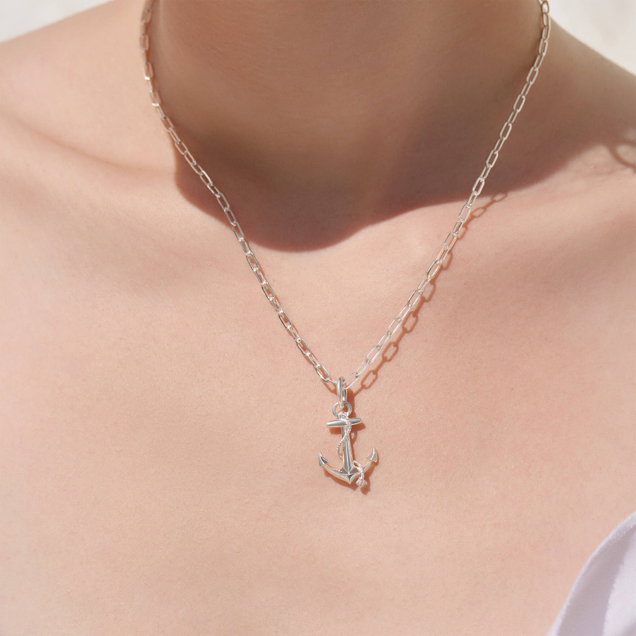 model wears handcrafted precious metal necklace pendant shaped like an anchor, symbolising strength and stability.