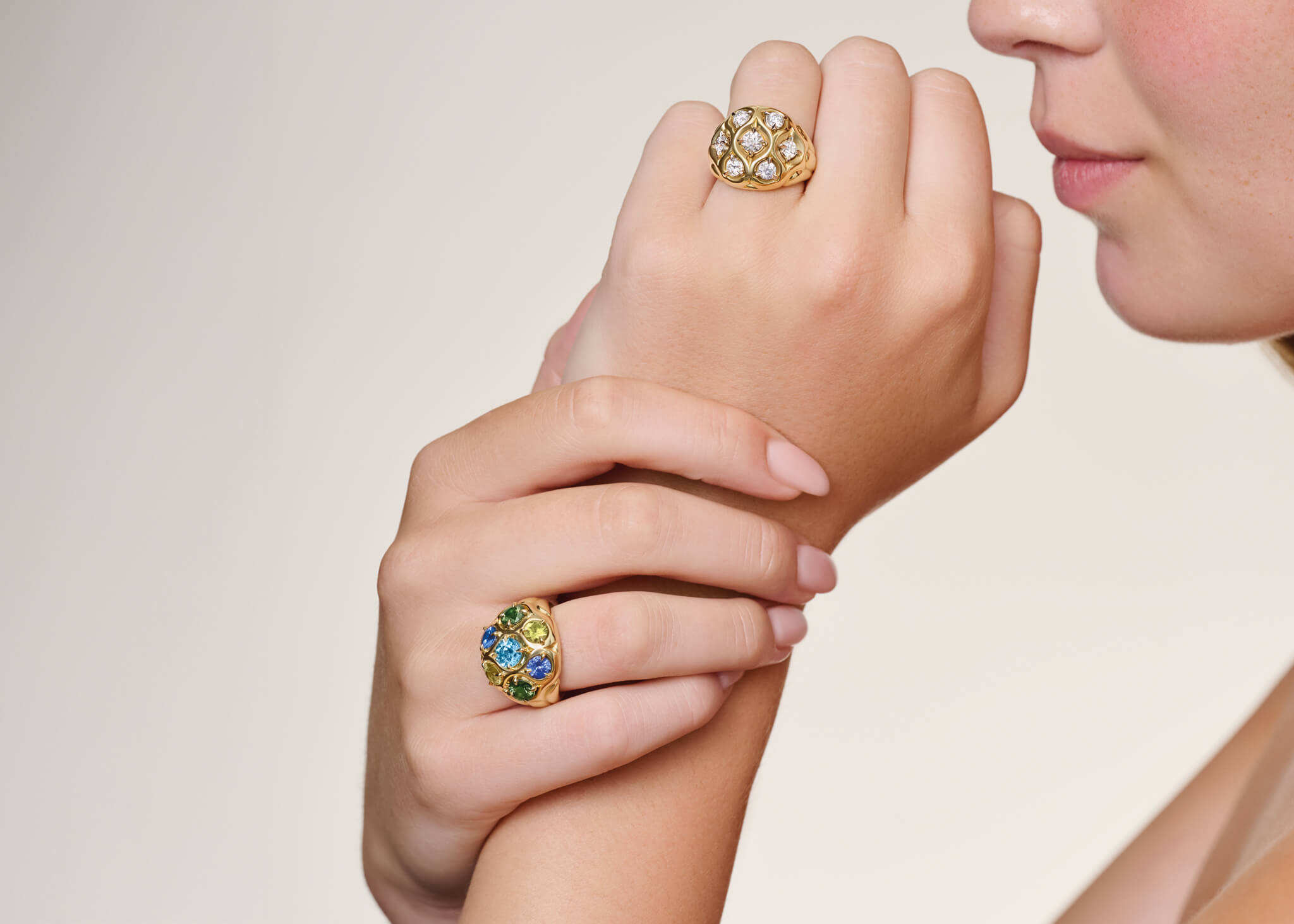 Close-up of a woman's hand wearing cocktail rings with gemstones on a neutral background