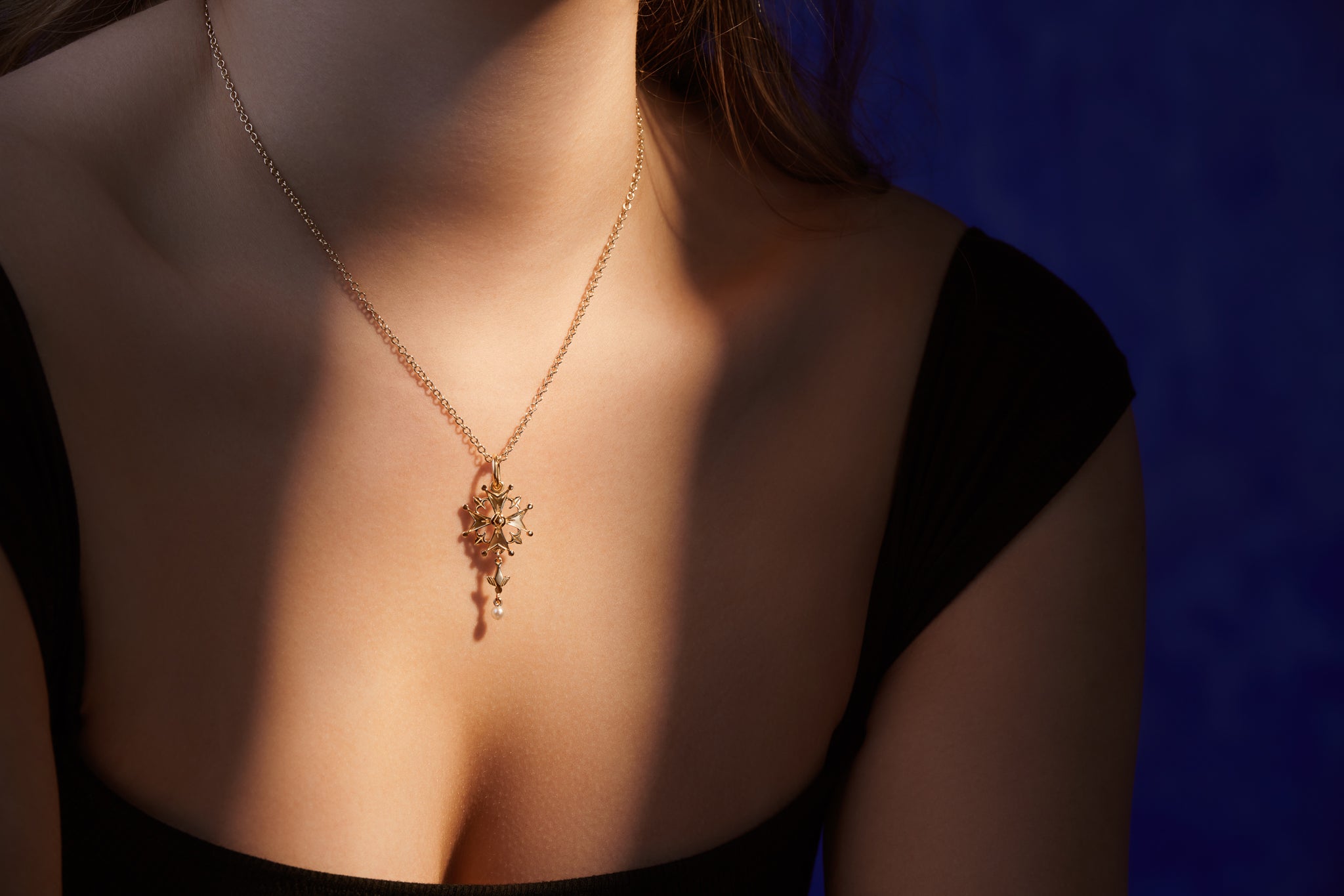 Model wearing a handcrafted yellow gold cross pendant featuring a Huguenot cross with a pearl at the bottom.