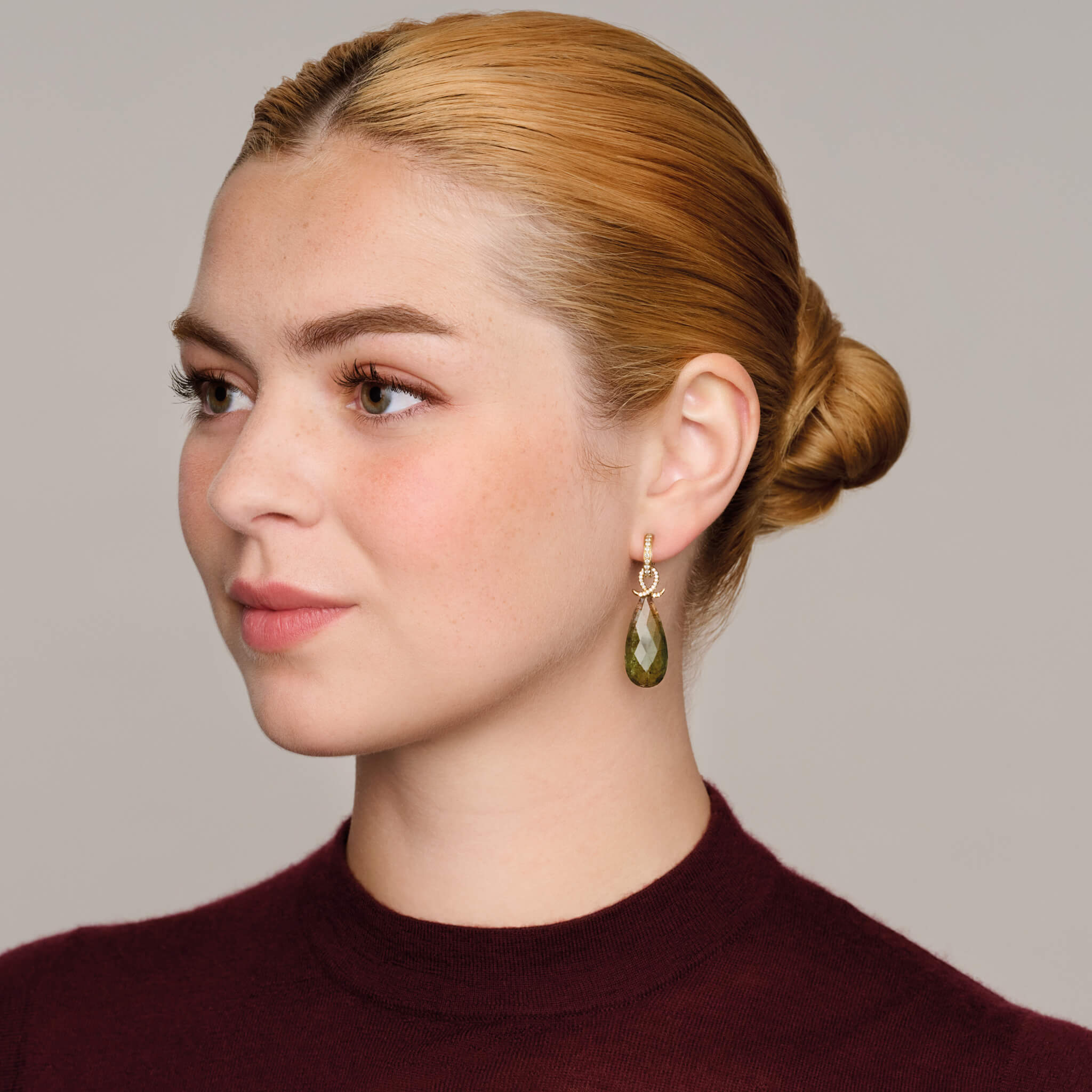 Model wearing handcrafted 18ct yellow gold earring drops with oval watermelon tourmaline and an oval loop shape crossing over.