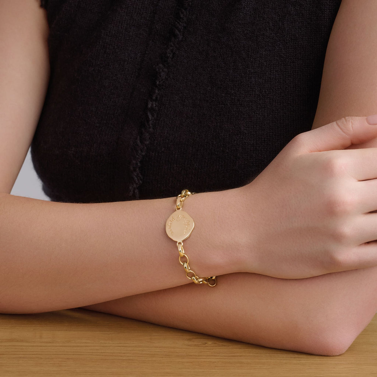 Model wears handcrafted yellow gold link bracelet featuring a round yellow gold pendant engraved with a quote