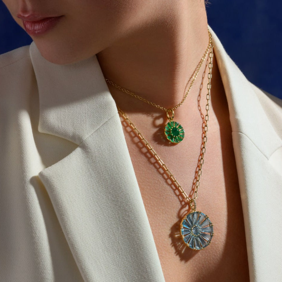 Model wearing two handcrafted necklace pendants in precious metal featuring a circular arrangement of precious stones.