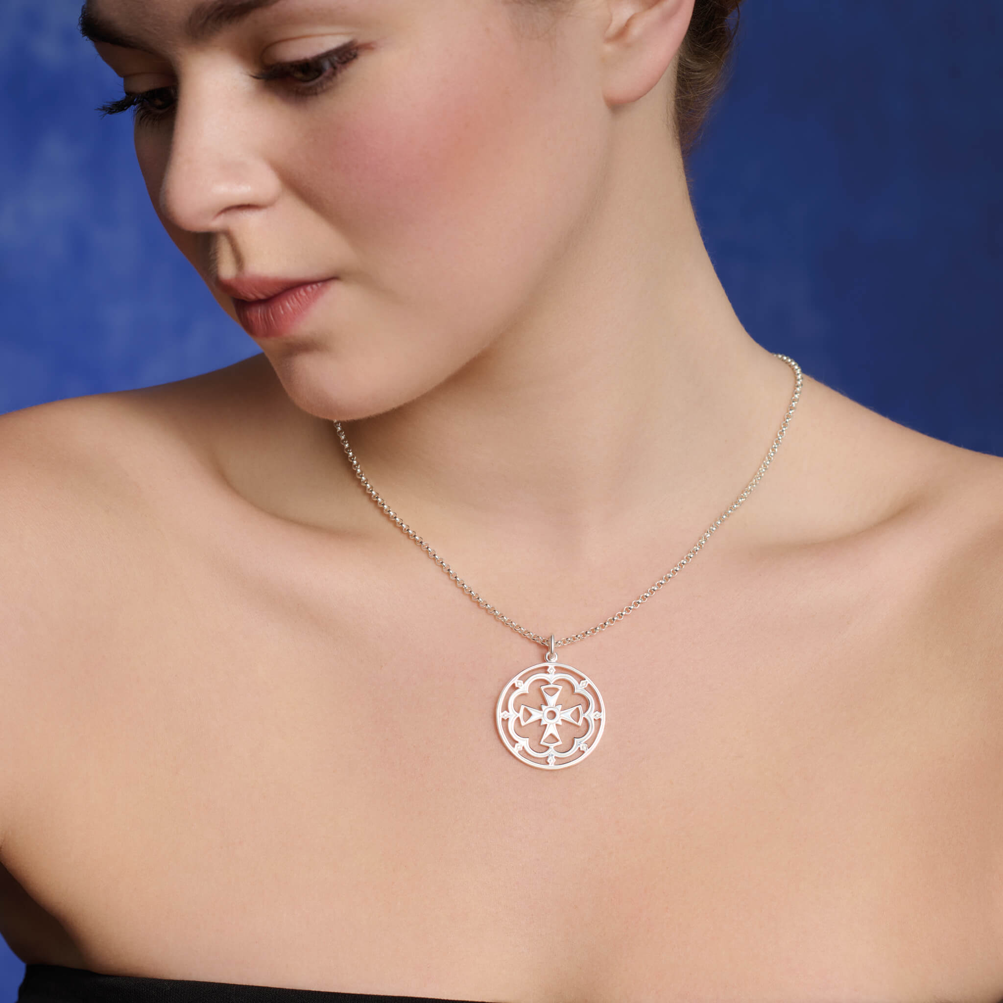 Model wearing large round precious metal pendant featuring a cross in the middle.