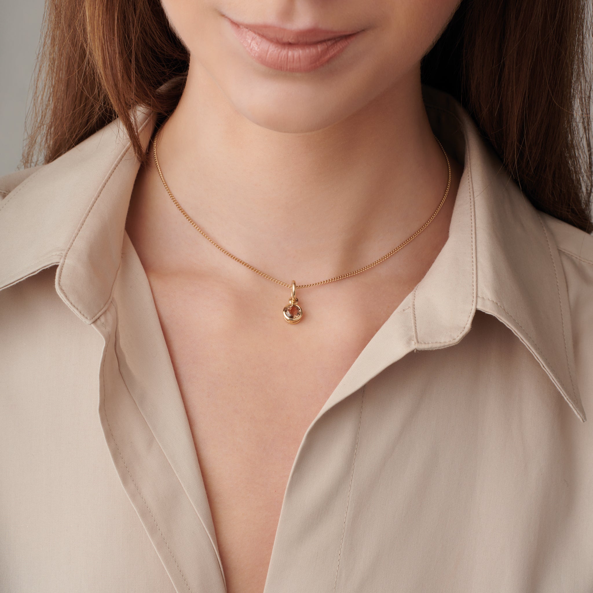 Model wearing a handcrafted necklace pendant in precious metal featuring a round precious stone.