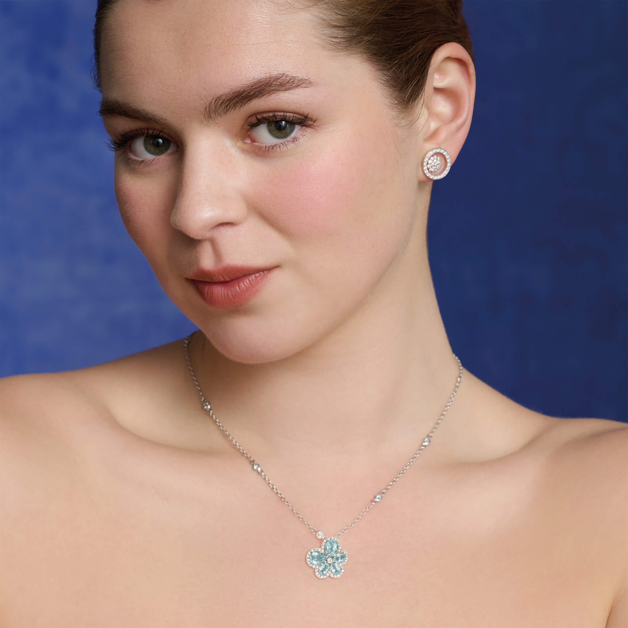 Model wears handcrafted 18ct white gold flower pendant with aquamarine petals and diamond accents, birthstone of March.
