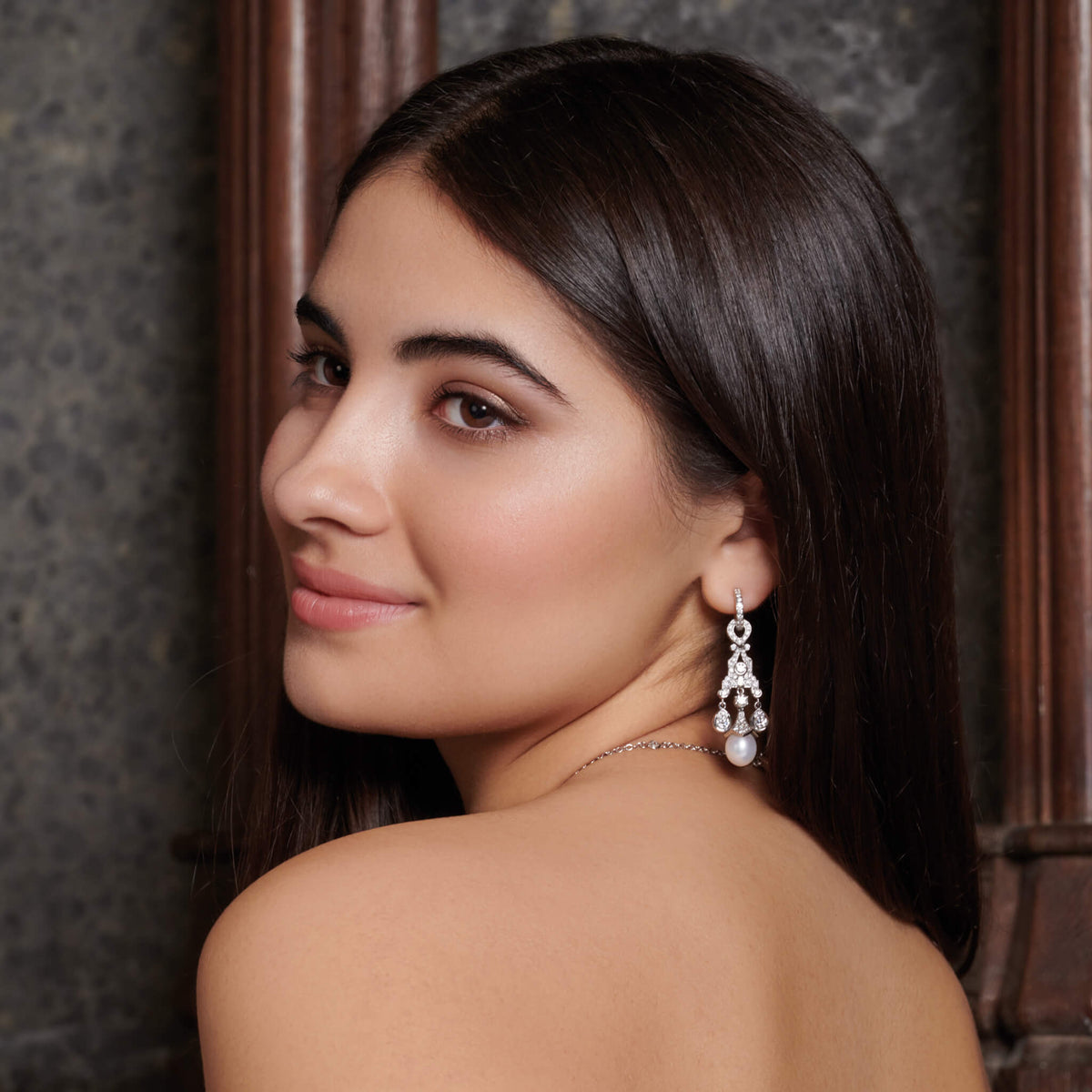 Model wearing handcrafted 18ct white gold earring drops featuring a teardrop shape with diamonds and a pearl at the bottom. The perfect bridal earrings.
