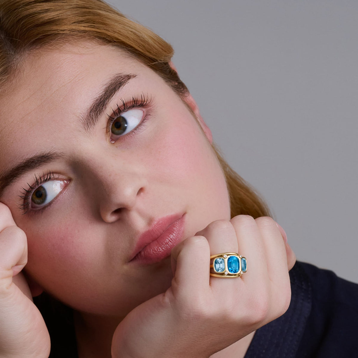 Model wearing a handcrafted 18ct yellow gold ring featuring rectangular shaped blue topaz and diamonds.