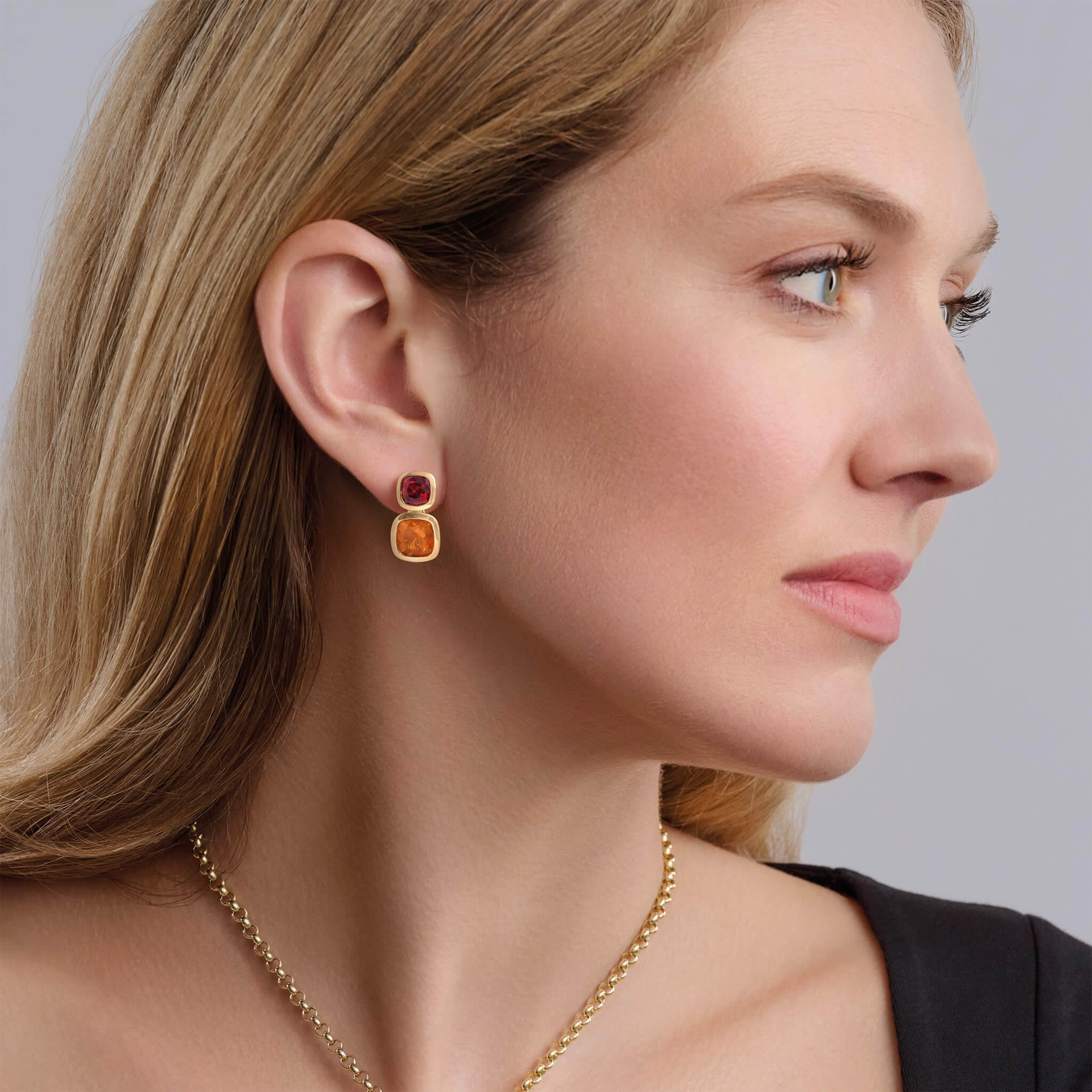 Model wearing handcrafted 18ct yellow gold square shaped earrings featuring rare facetted fire opal and garnet, birthstone of October and January