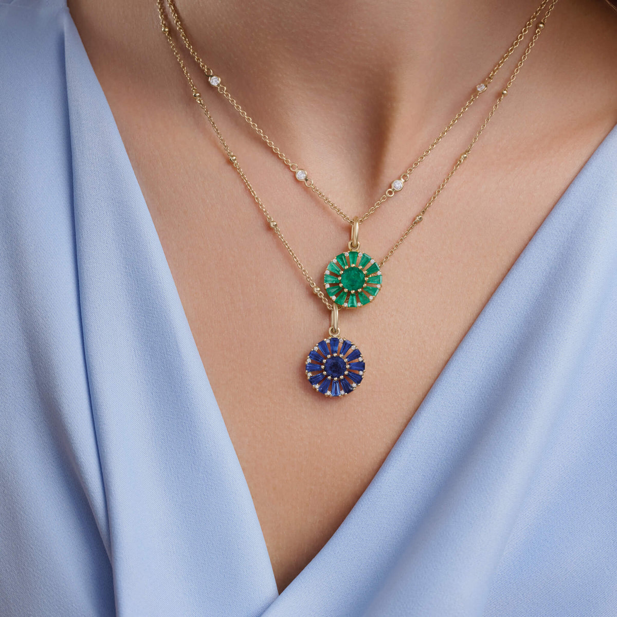 Model wears Roi Soleil small pendant with facetted baguette cut blue sapphire and fine green emerald, boh with diamond. The birthstone for May.