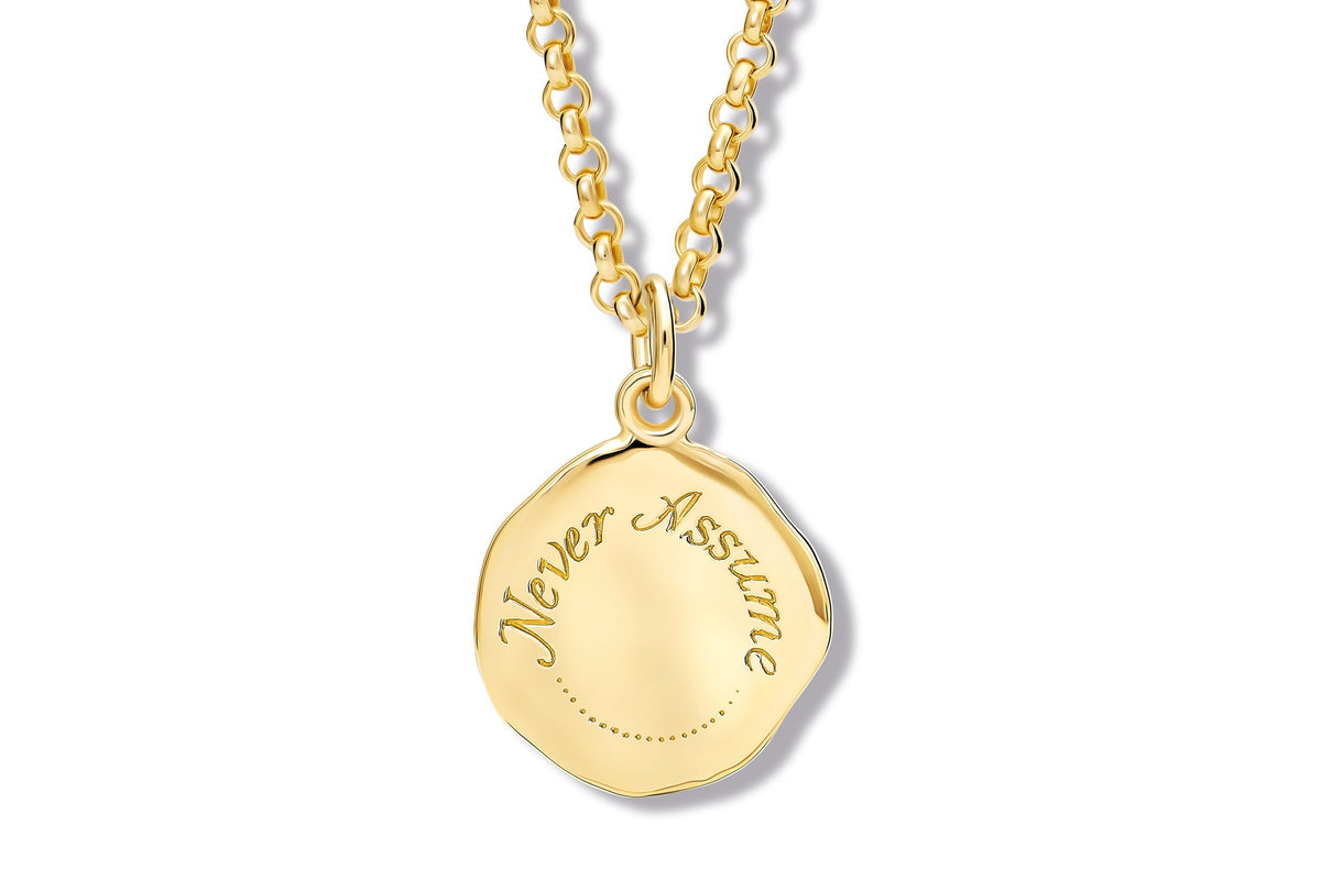 Handcrafted yellow gold disc pendant necklace engraved with the words 'Never Assume' 