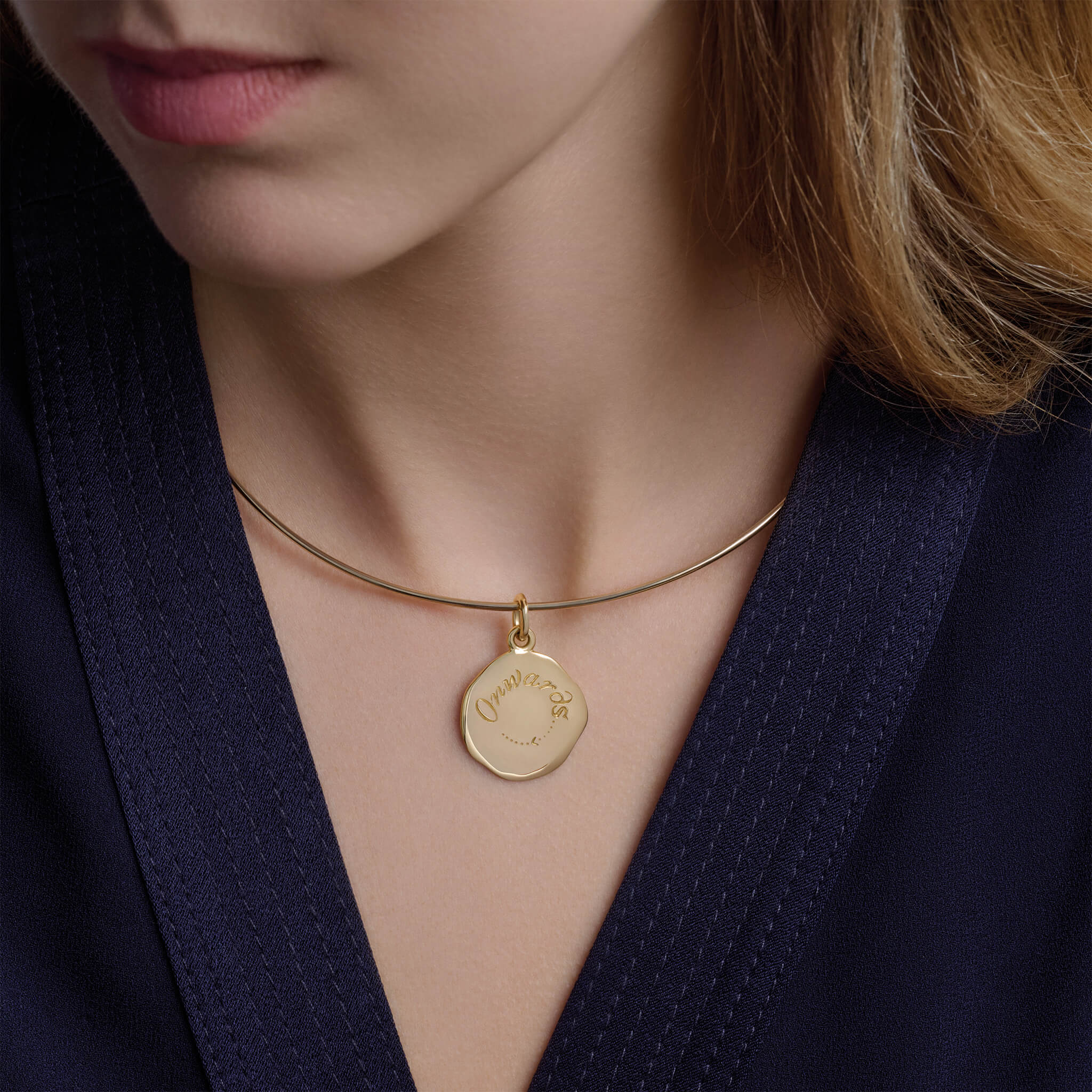 Model wearing a handcrafted round yellow gold pendant necklace engraved with a quote on courage.
