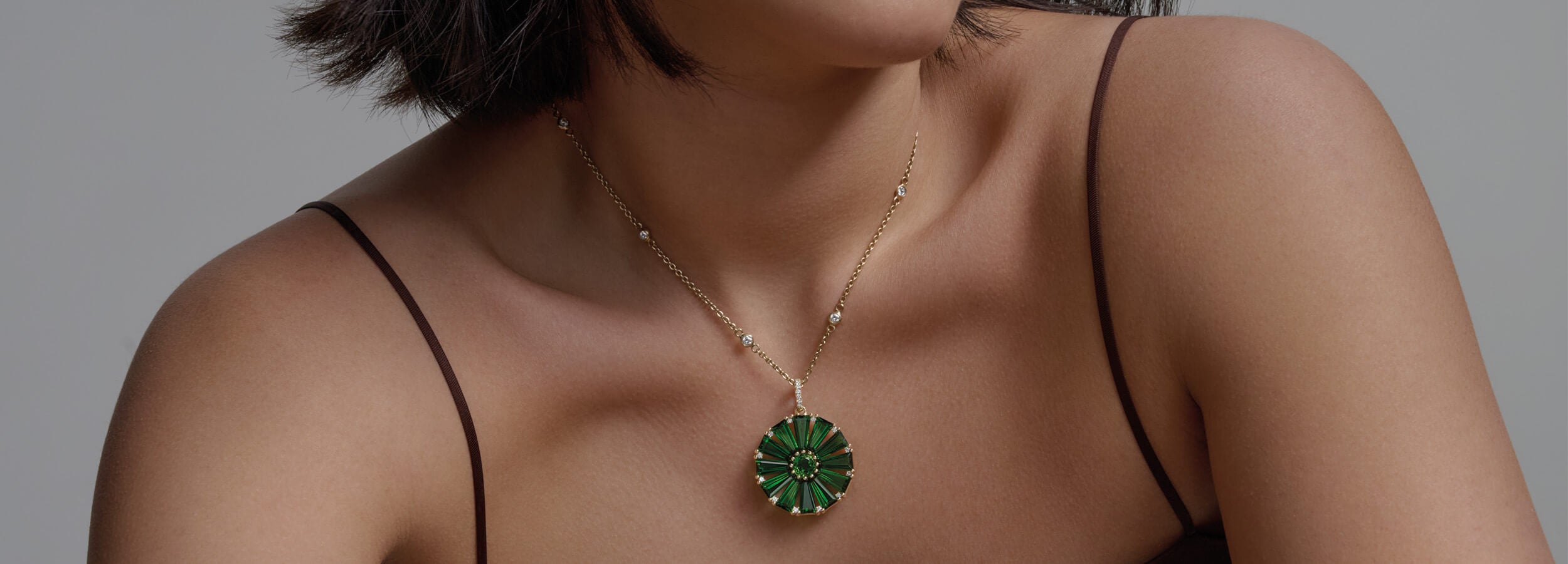 Model wearing a handcrafted yellow gold circular necklace pendant with baguette cut chrome diopside and diamond gemstones.