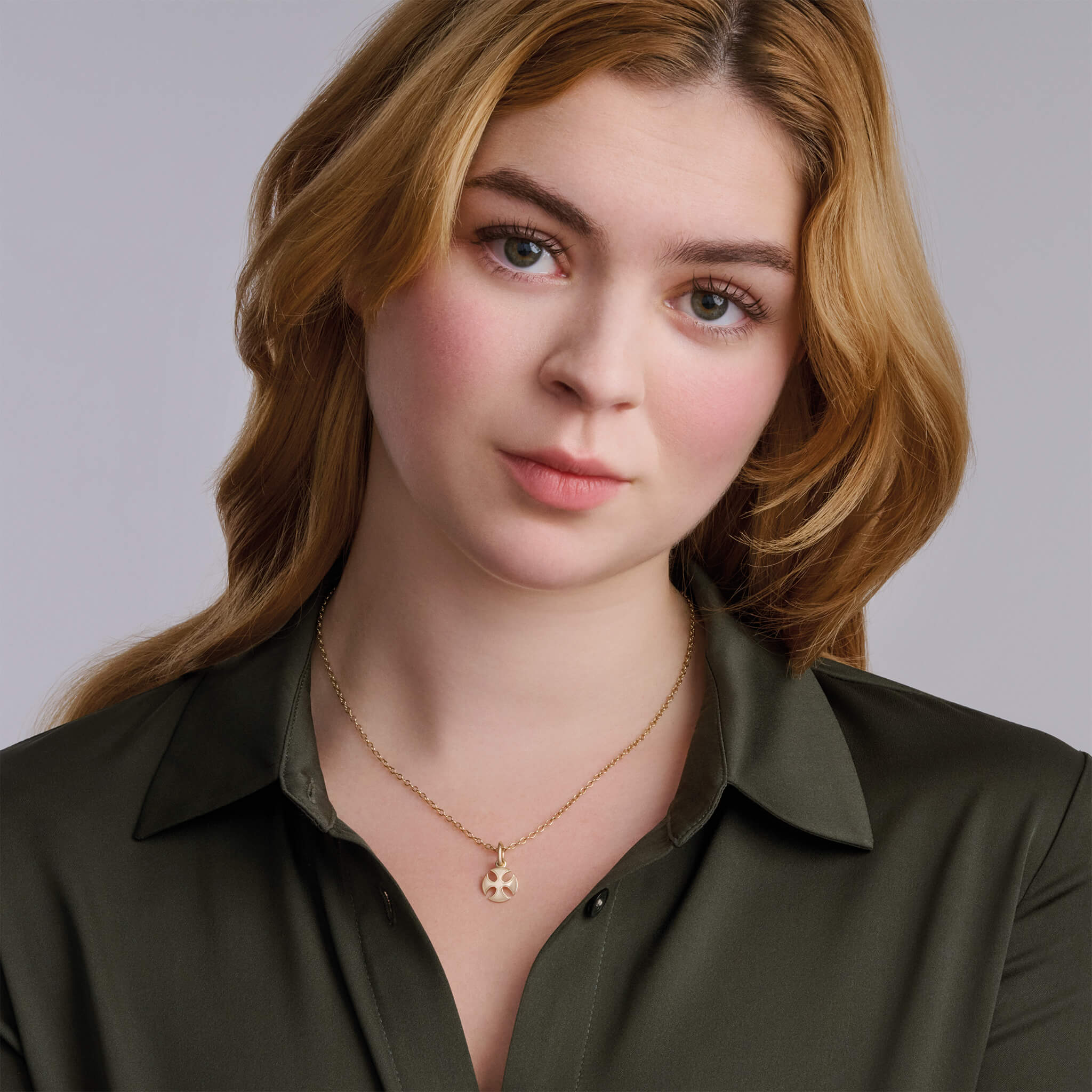 Model wears the handcrafted Sanctus precious metal necklace pendant in a curved cross shape.
