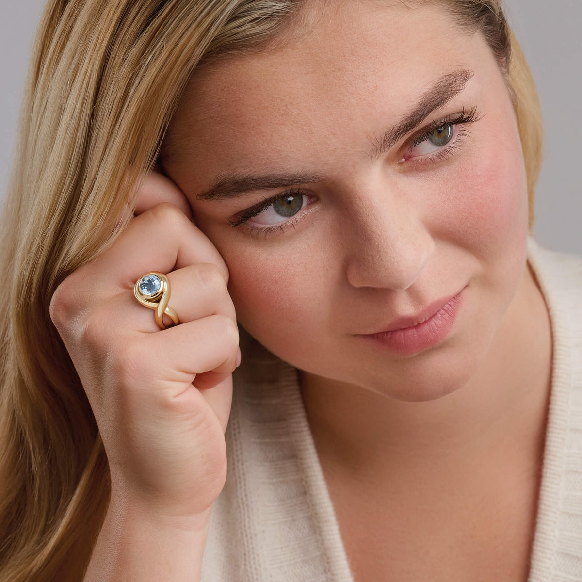 Model wears Handcrafted yellow gold ring featuring curved shanks with a round blue topaz, birthstone of November.