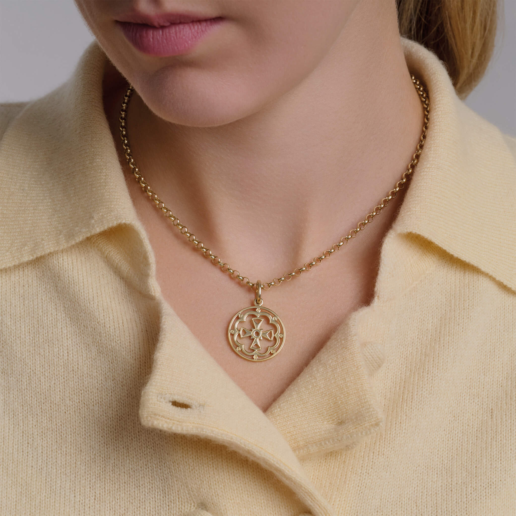 Model wearing round precious metal necklace pendant featuring a cross in the middle.