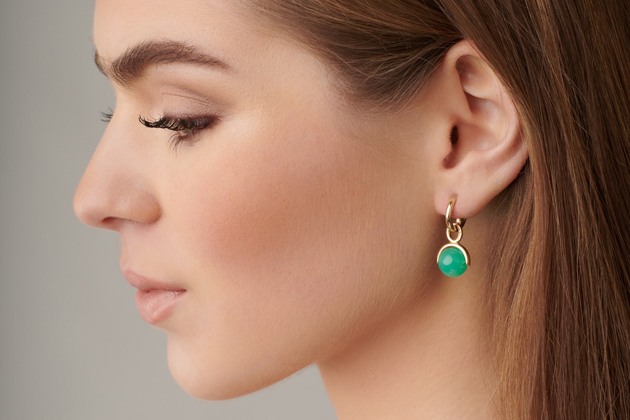 Model wearing handcrafted yellow gold earring drops featuring a precious gemstone, inspired by stirrups for equestrian activities.