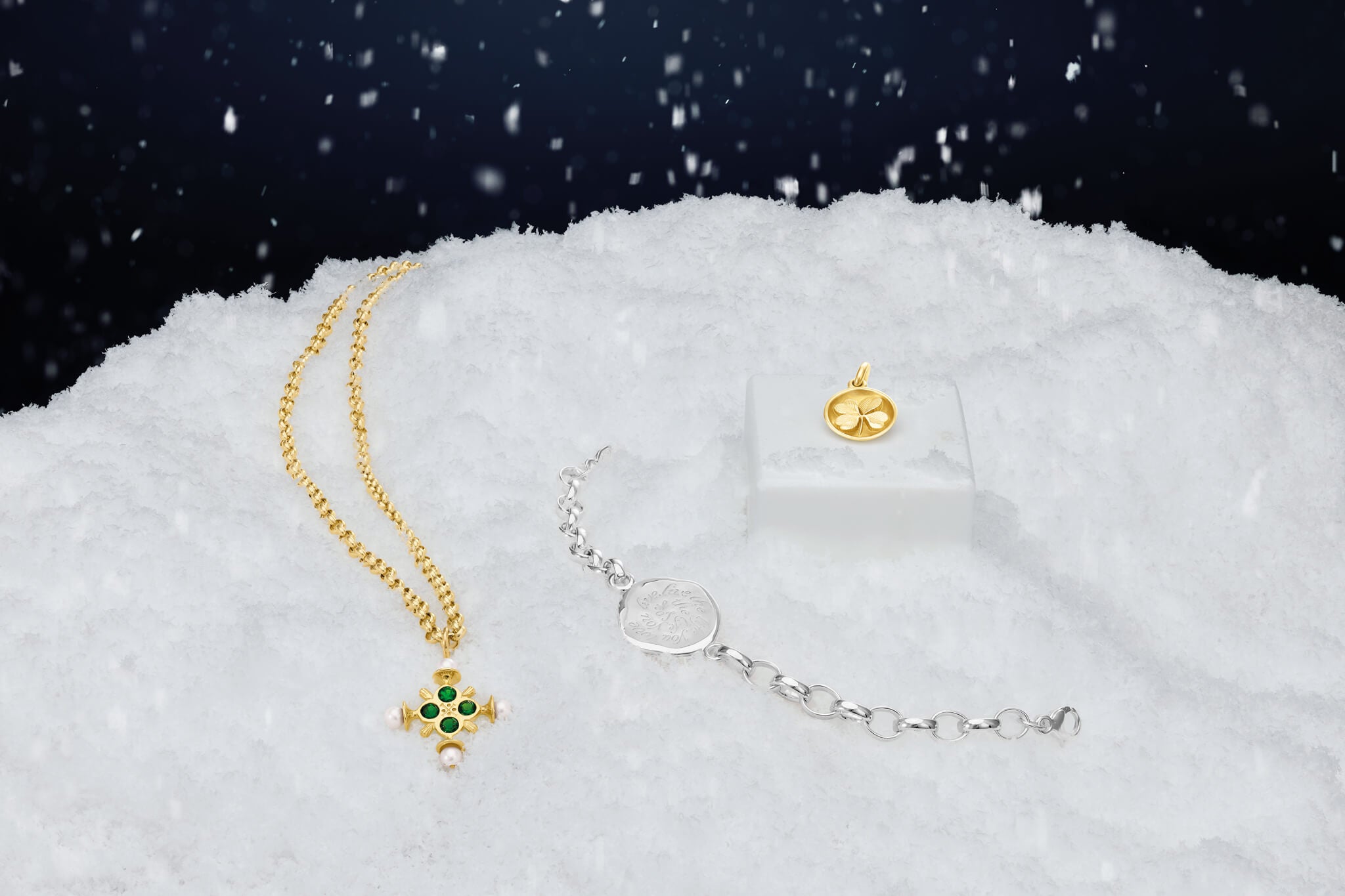 Gold necklace with green gemstones and silver bracelet on a snowy background
