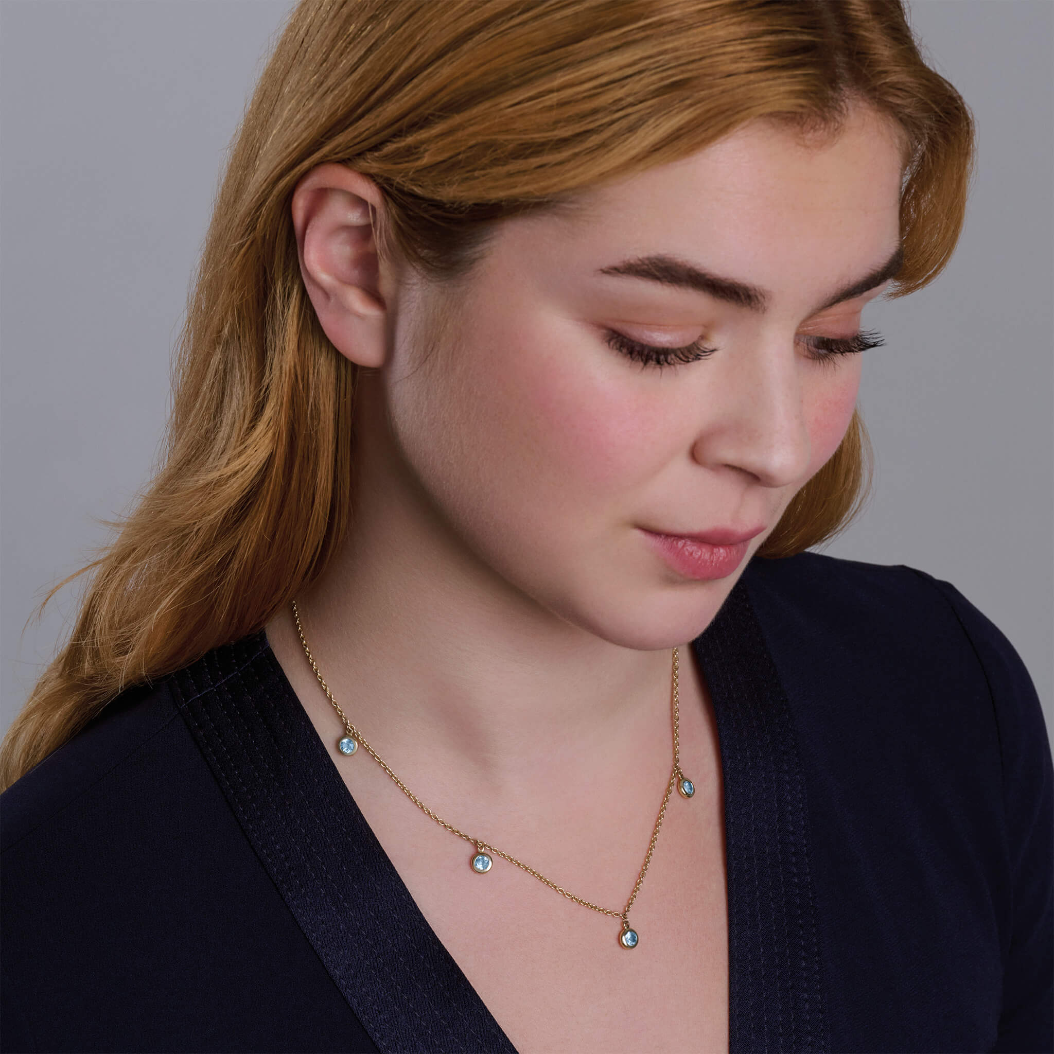 Model wearing a handcrafted necklace in precious metal with five round precious stone drops.